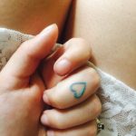 Tiny teal heart tattoo on the middle finger