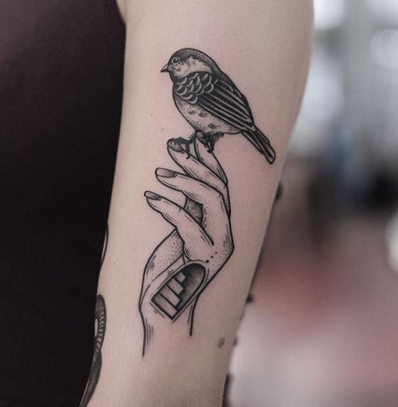 Hand holding a small bird tattoo
