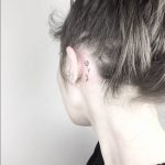 Small black flower behind the ear tattoo