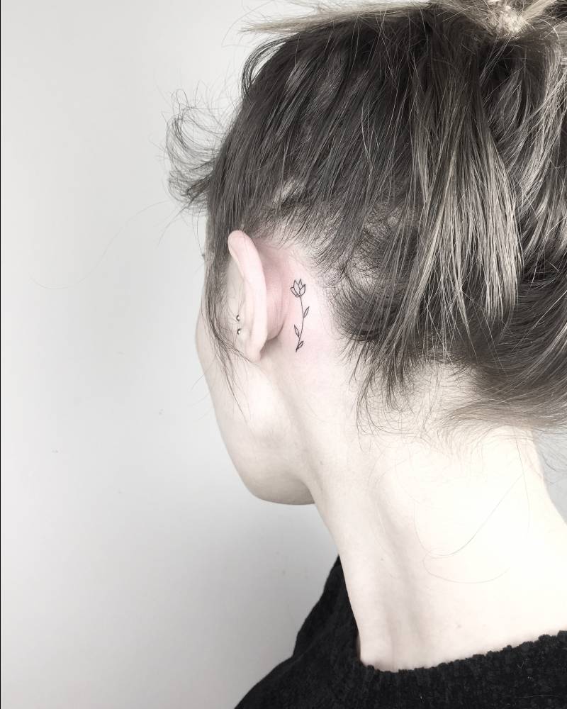 Small black flower behind the ear tattoo