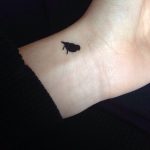 Tiny black bird tattoo on the wrist