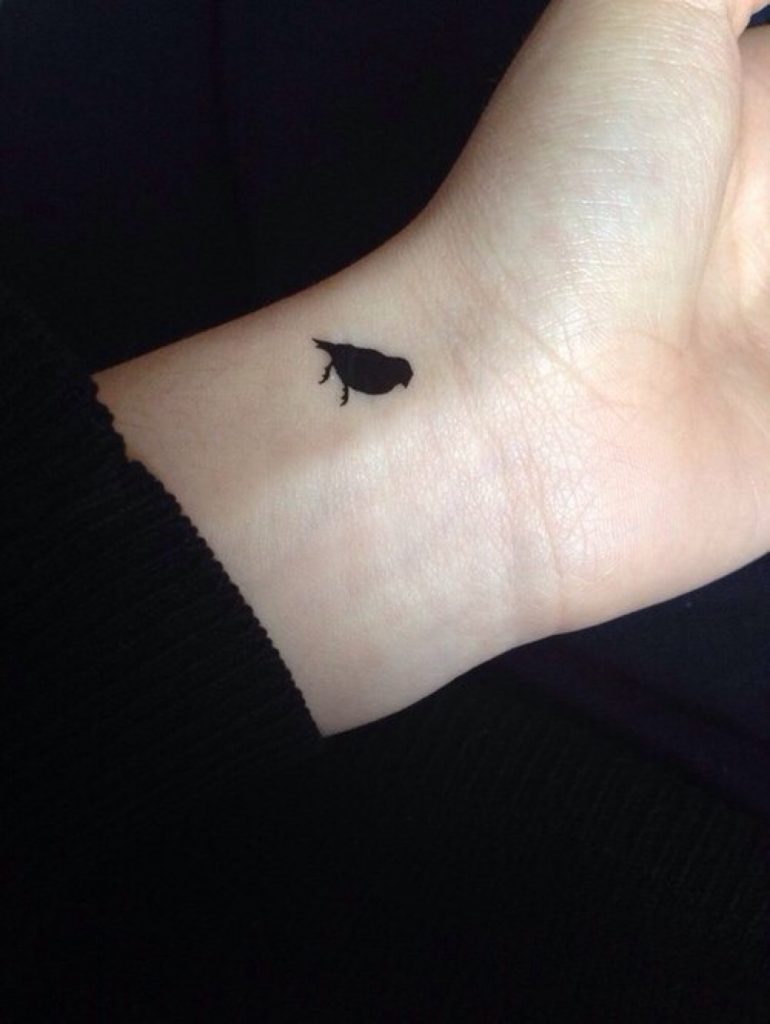 Tiny black bird tattoo on the wrist