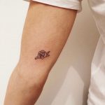 Tiny black rose tattoo on the inner arm