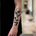 Black skull and rose tattoo on the forearm