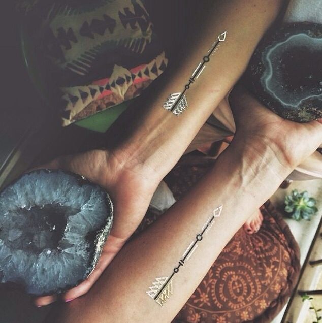 Matching arrow tattoos on inner forearms