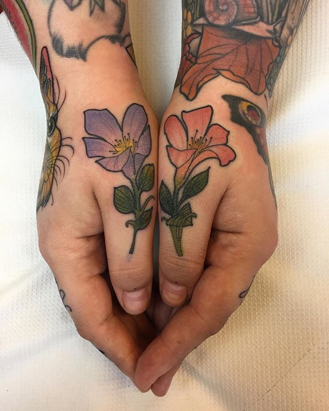 Matching violet and red flower tattoos on thumbs
