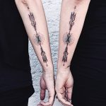 Matching stylized arrow tattoos on forearms