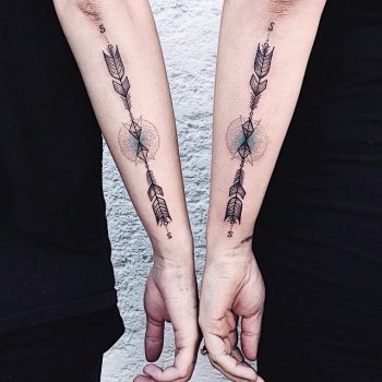 Matching stylized arrow tattoos on forearms