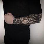 Black floral ornament tattoo on the left forearm