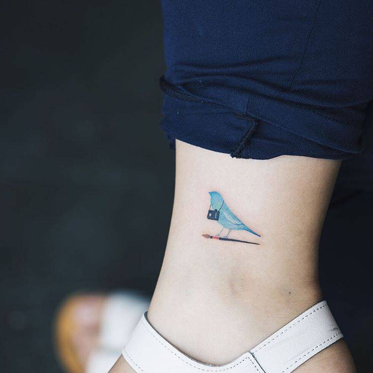 Tiny tattoo of a blue bird on an ankle 