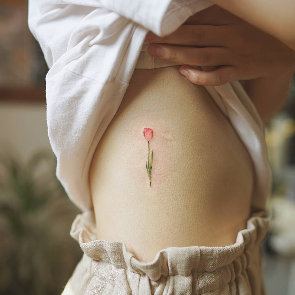 Tiny red tulip tattoo on the rib