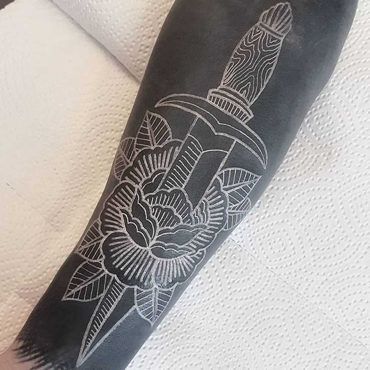 Negative space flower and dagger tattoo