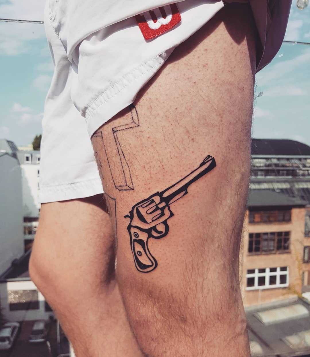 Black and white revolver tattoo on the thigh