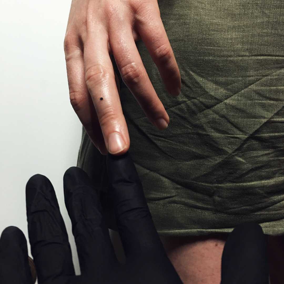 Tiny dot tattoo on the middle finger