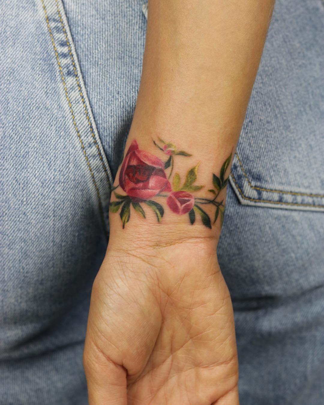 Fine line flower bracelet tattoo on the forearm.