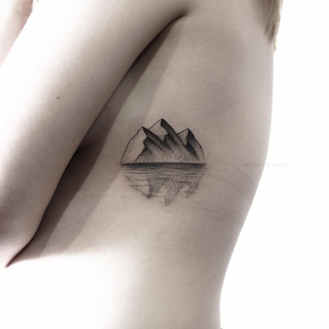 Reflection of mountains in water tattooed on the left rib cage by Evgeny Me...